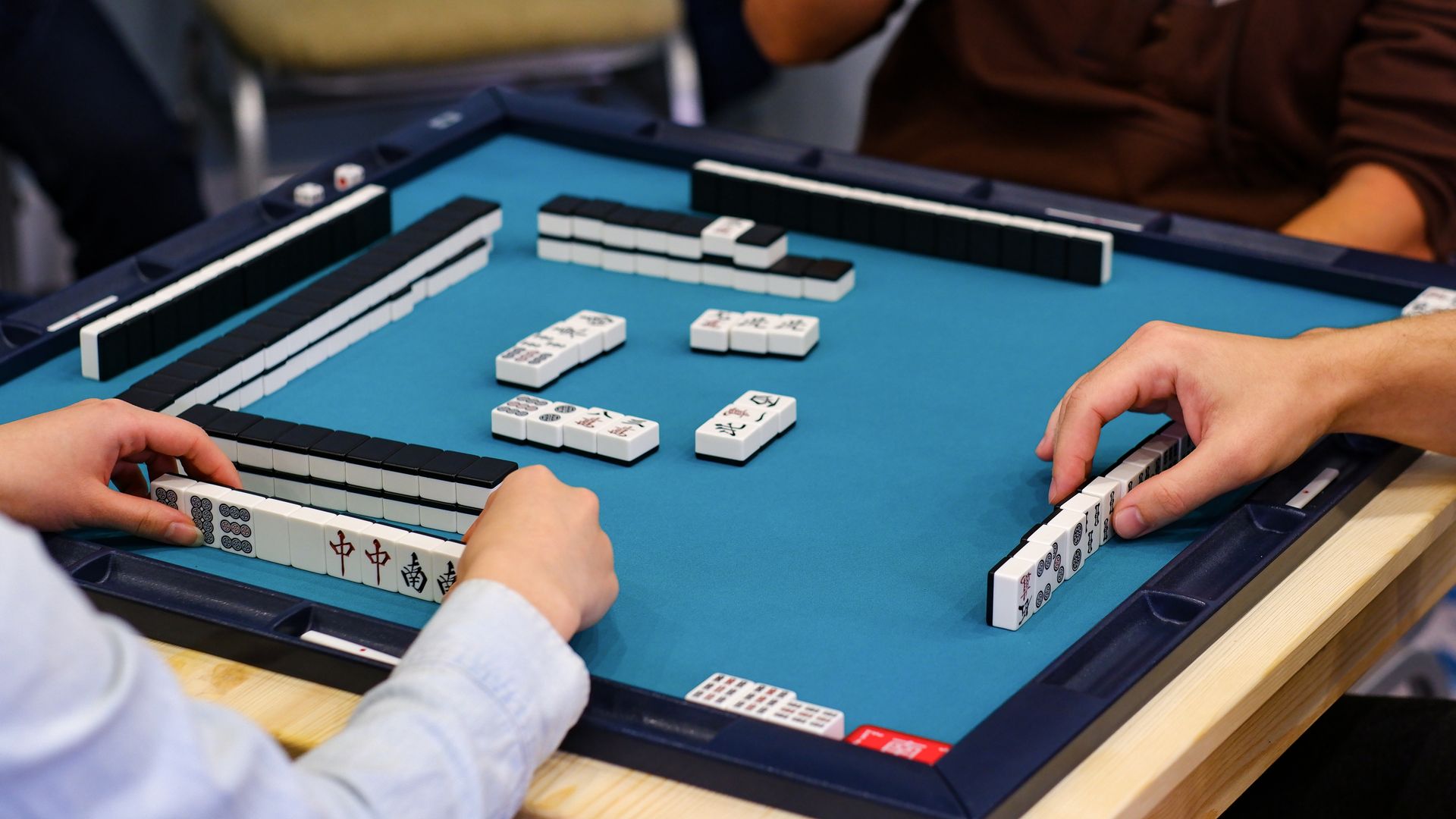 Close-up of players' hands at a blue-felted mahjong table during a game